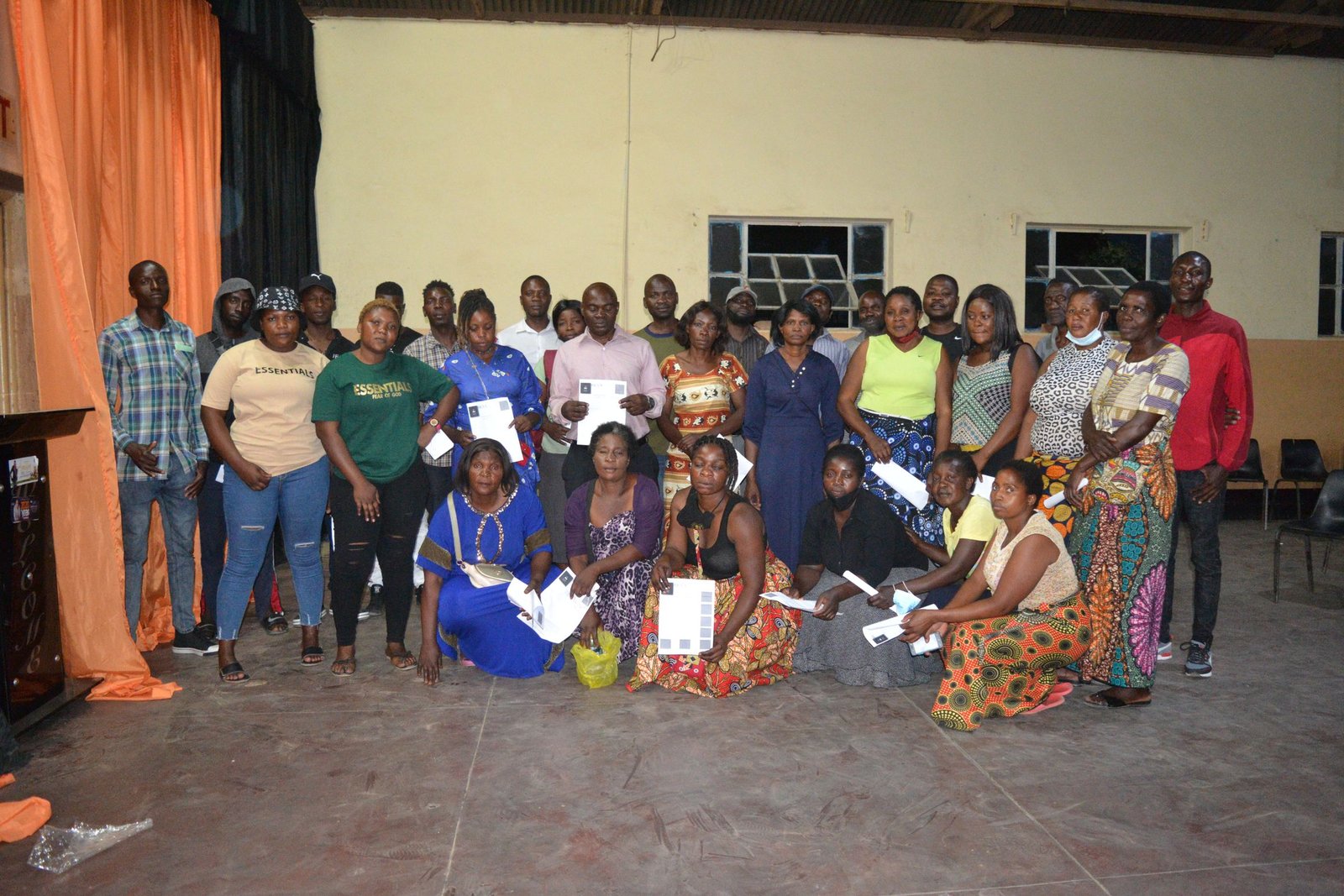A large group of adults posed together in a hall, many holding certificates