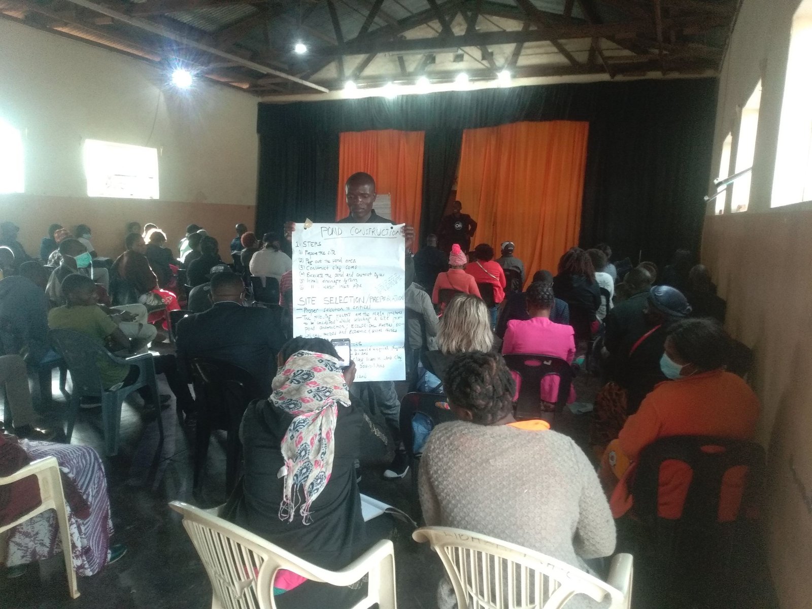 People seated in a wide circle of chairs in a hall during a group workshop