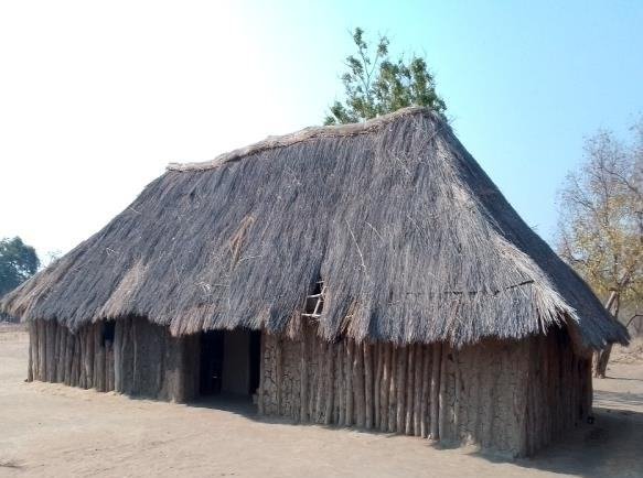 A thatched mud-and-pole classroom block standing on bare sand at Napakwe Primary School